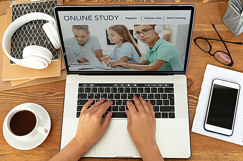 Top view of young adult hands typing on laptop keypad surrounded by business supplies