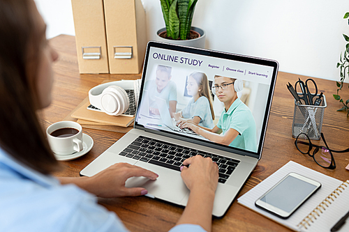 Young woman surfing in the net while using website of distant learning for schoolchildren in front of laptop