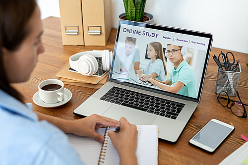 Young woman making notes while looking at laptop display and surfing in the net for educational information