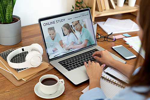 Young woman touching laptop keypad while surfing in the net for online educational data by desk