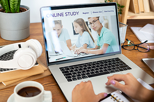 Laptop with homepage of educational website on display being used by young female student by desk