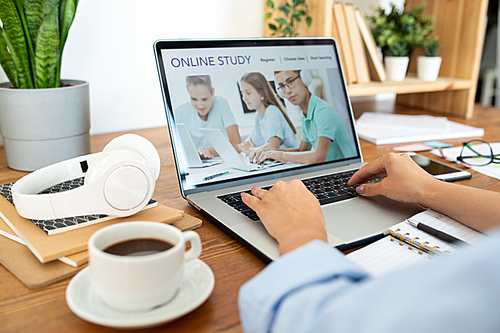 Female hands pressing keys of laptop keypad while sitting by desk in front of display at home or in office