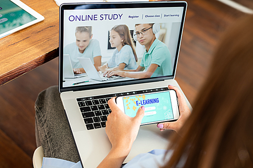 Young female student holding smartphone over laptop keypad while registrating on educational website