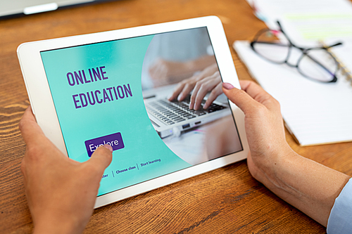 Female hands holding touchpad over wooden table while going to explore educational website