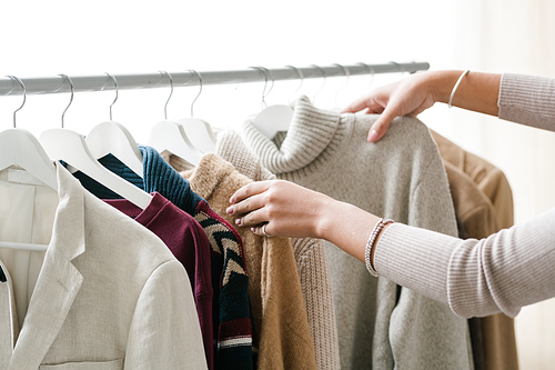 Hands of young female shopper choosing warm knitted and woolen clothes from new seasonal casualwear collection