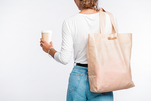 Back view of young woman in casualwear carrying glass of coffee in hand and tote bag over shoulder