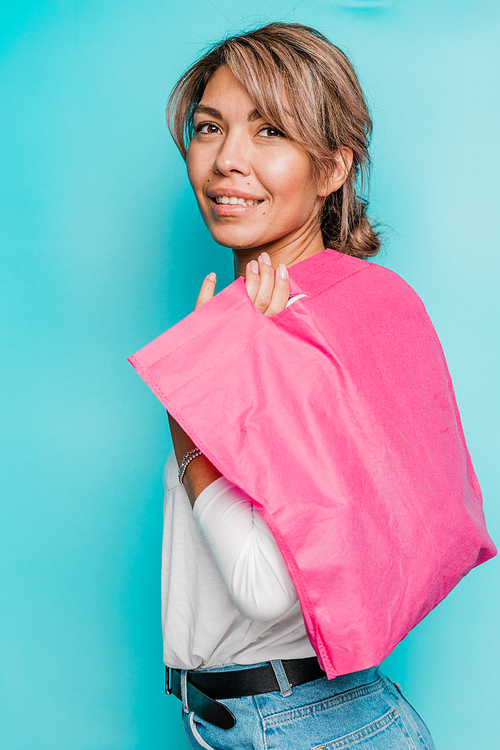 Young smiling woman in casualwear holding bright pink textile bag on shoulder while standing in front of camera