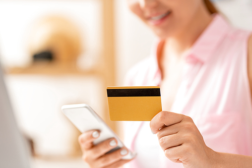 Contemporary female shopper entering data from plastic card in smartphone while making online order