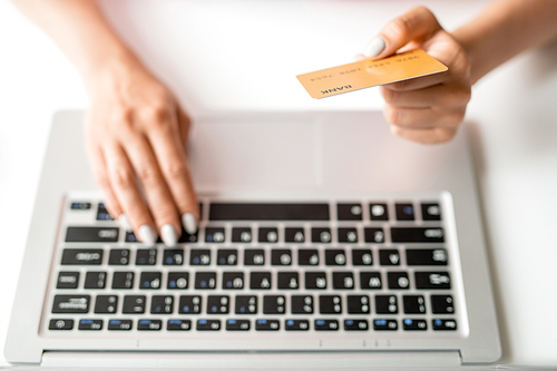 Hand of female online shopper holding plastic card over laptop keypad while entering its number to pay for order
