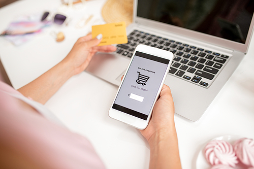 Smartphone held by young contemporary mobile shopper searching for goods to add new ones in basket