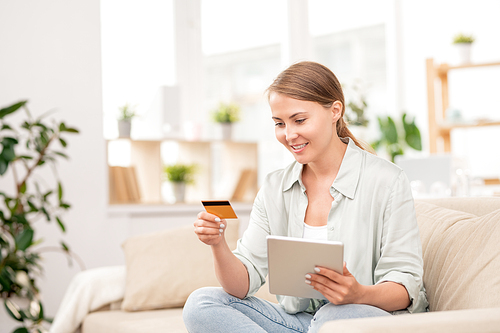 Young casual female shopper looking at personal data on plastic card while going to pay for online order