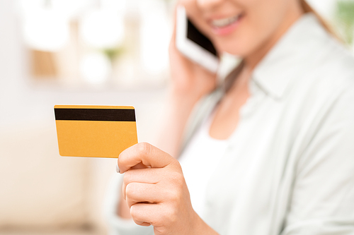Yellow plastic card with black magnet line in hand of young female consumer talking by smartphone