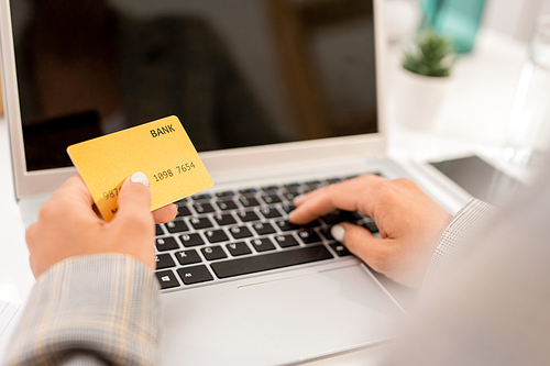 Modern businesswoman entering personal data from plastic card after making order in online shop at workplace