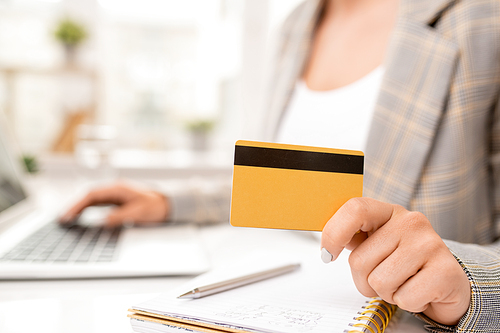 Yellow credit card with black magnet line held by young contemporary businesswoman over page of notebook during work