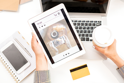 View of tablet with screensaver of online shop held by businesswoman with drink by workplace