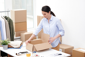 Manager of online shop opening empty box before packing new casualwear for client and putting them there