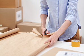 Young casual female worker of online shop office cutting paper for wrapping packages with clients orders