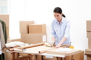 Manager of online shop office standing by workplace while cutting wrapping paper to pack orders of clients