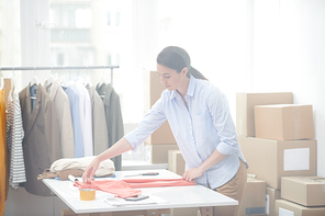 Young office manager of online shop preparing casualwear for one of clients while folding it up before packing