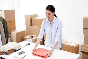 Pretty online shop manager preparing one of orders of clients and folding pullover before packing it