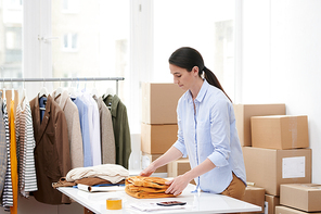 Young manager folding one of items of new seasonal casualwear collection while preparing it for packing