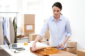 young manager of online shop wrapping folded yellow pants into paper while packing it before sending to client