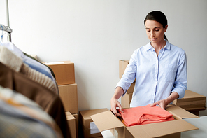 Young casual employee putting folded casualwear into box in process of packing client order in office