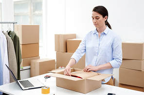 Manager of online shop packing goods into wrapping paper and carton box before sending the parcel to client