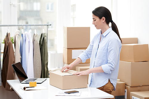 Young manager of online shop packing box with casualwear while preparing it for sending to client