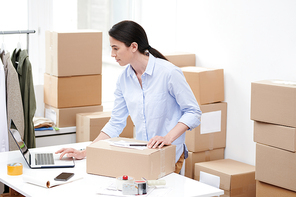 Busy manager of oline shop with packed box looking at order information on laptop display before sending it