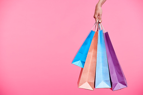 Four colorful paperbags held by hand of female shopaholic while carrying them after shopping