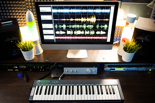 Piano keyboard and computer screen with waveform sound visualization on workplace of modern musician or deejay in studio