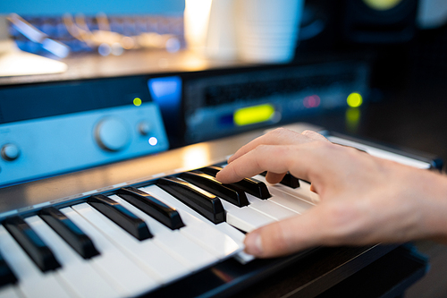 Hand of pianist pressing one of keys of piano keyboard while recording music in contemporary studio