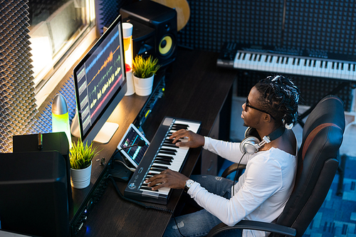 Young musician of African ethnicity sitting in studio of recording, making new music and mixing sounds in computer
