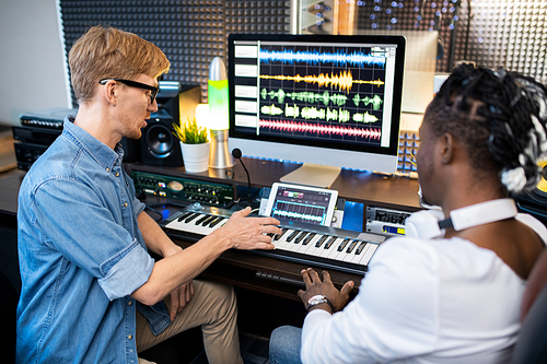 Two young multicultural musicians discussing new way of mising sounds while working over recording music in studio