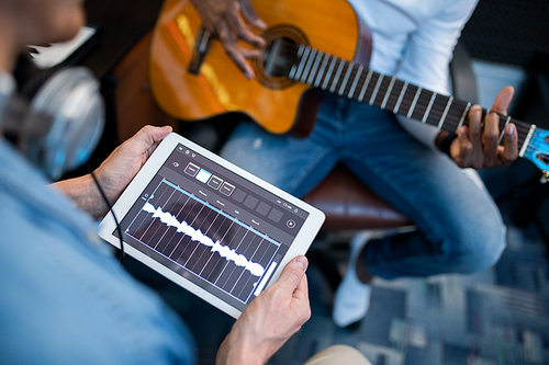 Digital tablet with sound waveforms on its display held by young contemporary musician during recording process