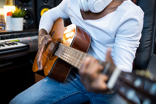 Acoustic guitar in hands of young musician of African ethnicity during process of singing and sound recording in studio