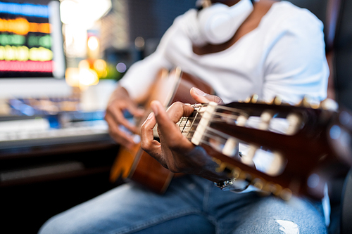 Hands of young musician of African ethnicity on strings of acoustic guitar during process of singing or sound recording