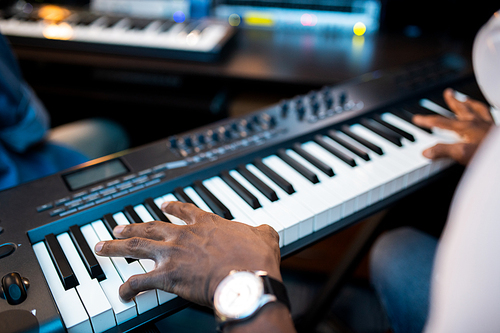 Hands of young African composers or musician touching keys of pianoboard while working in sound recording studio