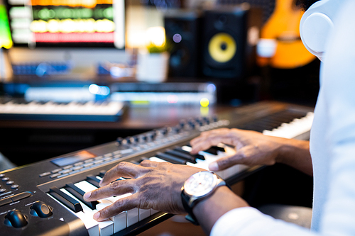Hands of young African-american musician over keys of pianoboard working alone in contemporary sound recording studio