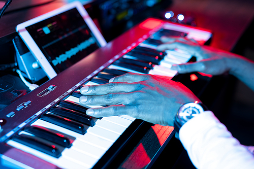 Hands of young contemporary musician over keys of pianoboard during process of making music and sound recording