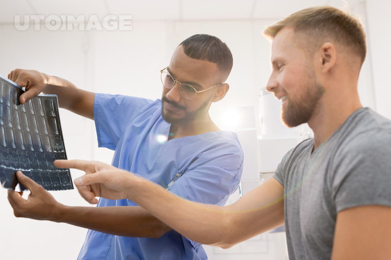 유토이미지 | Radiologist in blue uniform and his patient discussing x-ray of broken joint while one of men pointing at it in... 