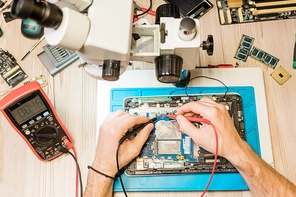 Overview of hands of professional repairman with small soldering-irons during work with tiny details of broken gadget