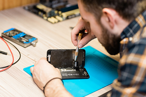 Professional gadget repair service master holding cover of smartphone while fixing tiny details with special screwdriver