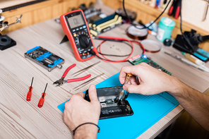 Hands of gadget repair service master using screwdriver while fixing tiny details of demounted smartphone