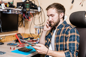 Master of gadget repair service phoning one of clients while looking through online data in touchpad