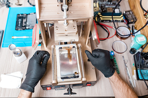 Overview of gloved hands of professional repairman using equipment for gadget repair while carrying out his work