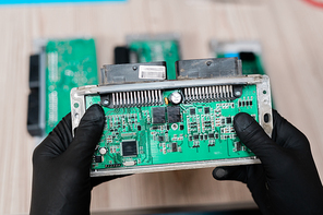 Gloved hands of professional repairman holding part of demounted gadget over workplace while working with it