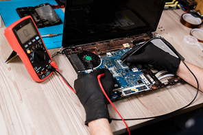 Gloved hands of contemporary master of gadget repair service using two small soldering-irons while working over broken laptop