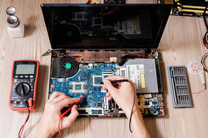 Hands of contemporary technical repairman using two small soldering-irons to repair broken laptop